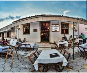 Fachada do restaurante Empório, em casa colonial branca, com mesas e clientes sentados ao ar livre na calçada, ilustrando a gastronomia de rua de Pirenópolis.