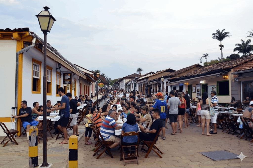 Rua íngreme e movimentada do centro histórico de Pirenópolis, com mesas de restaurantes cheias de pessoas ao ar livre e carros estacionados, destacando o forte comércio e vida social da cidade.
