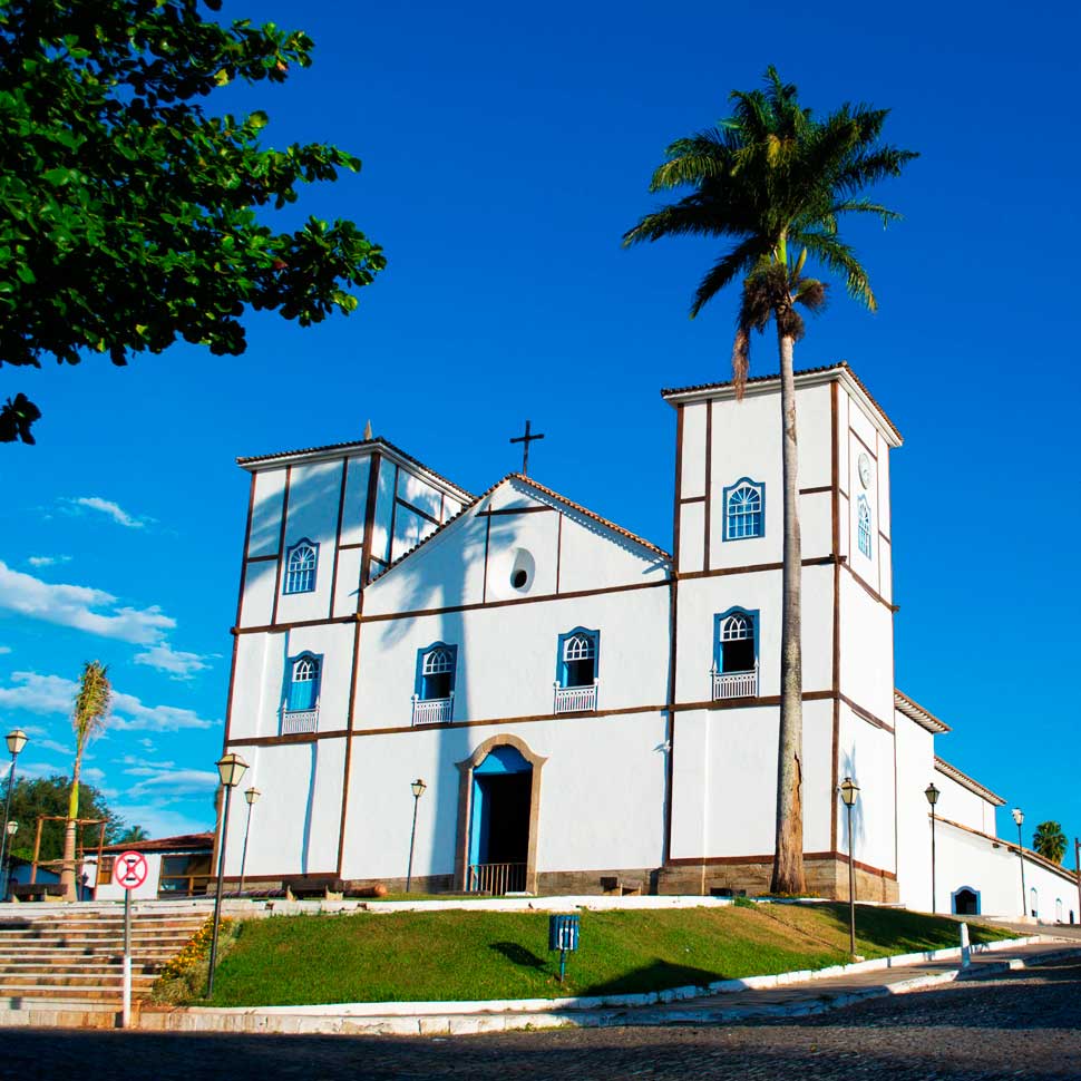 Igreja Matriz de Nossa Senhora do Rosário, com fachada branca e detalhes azuis e duas torres, sob céu limpo. Ponto turístico e arquitetura colonial de Pirenópolis.
