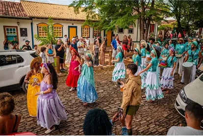 Grupo de dançarinos com trajes coloridos em evento cultural na rua de paralelepípedos do centro histórico de Pirenópolis, com casas coloniais ao fundo.